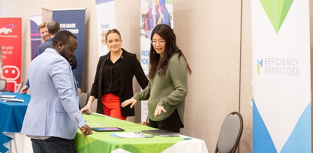 Two women standing behind booth and a man talking to them.